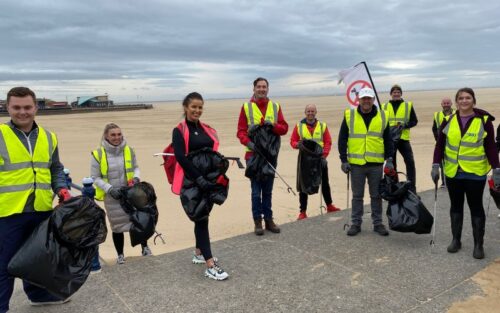 People in high vis yellow jackets with litter pickers and a beach in background