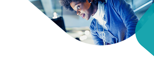 A black woman in an office setting looking at a desk and monitor