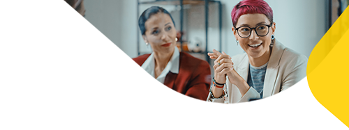 Two women in view in a meeting room setting smiling.